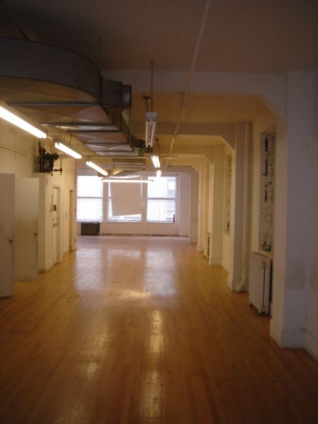 Empty loft with wooden floor, white walls, exposed ductwork, and large windows.