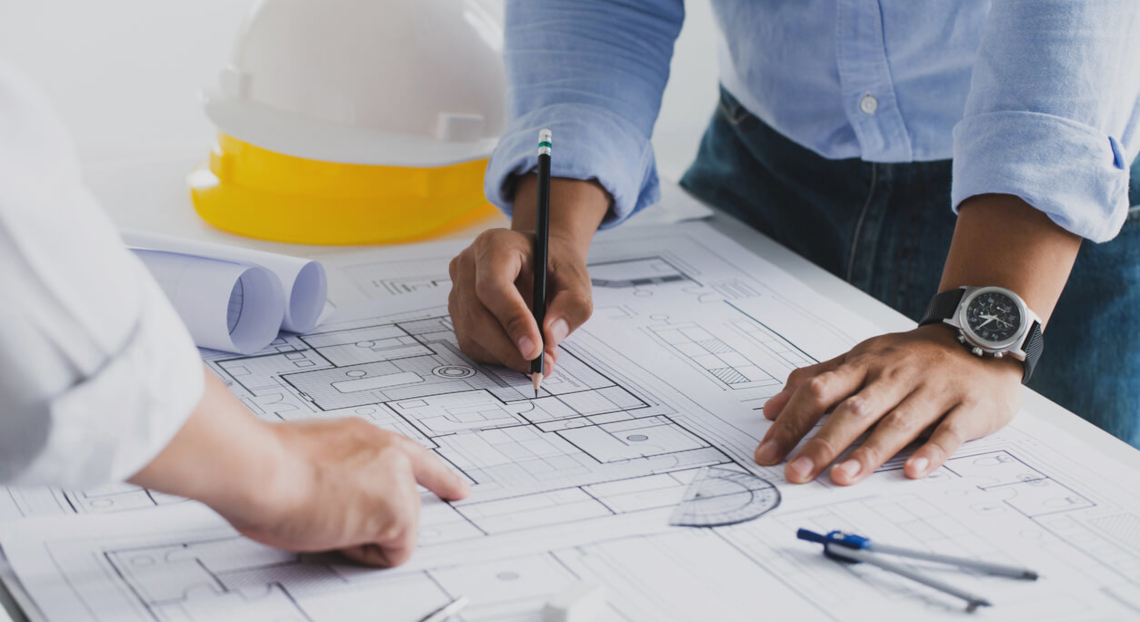 Architect & engineer brainstorm at office desk, reviewing blueprints for a construction project