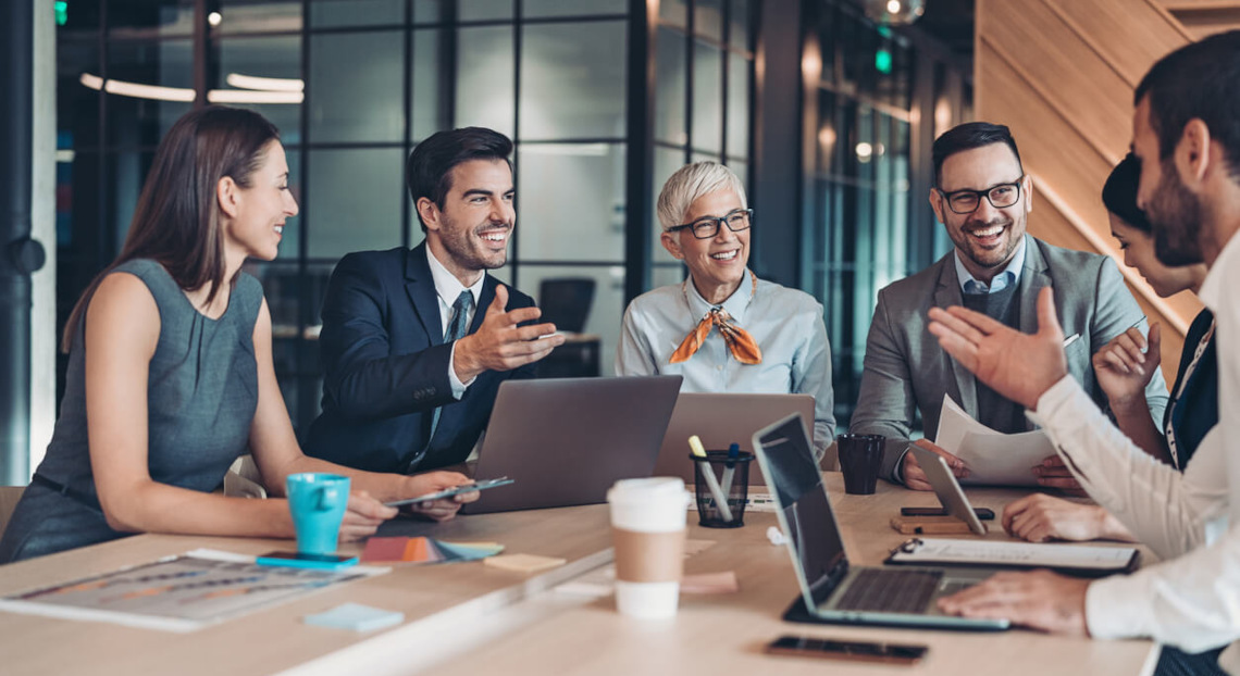 A diverse group of professionals gathered around a table, sharing a laugh during a meeting.