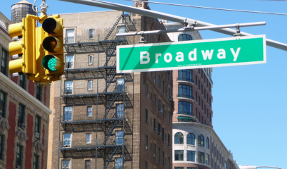 Broadway street sign with a green traffic light and multiple buildings visible in the background