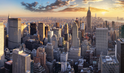 Panoramic view of the New York City skyline at sunset. Tall buildings cast long shadows.