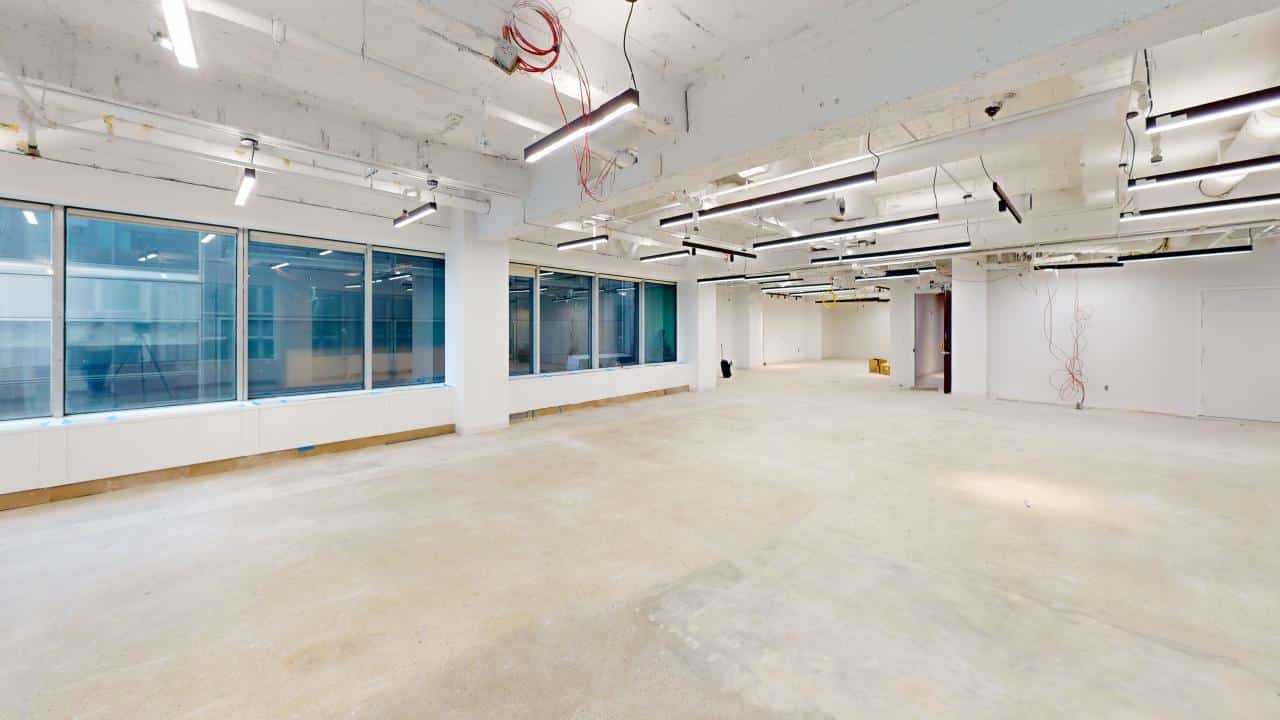 A spacious, unfinished office with concrete floors and large windows filling one wall.