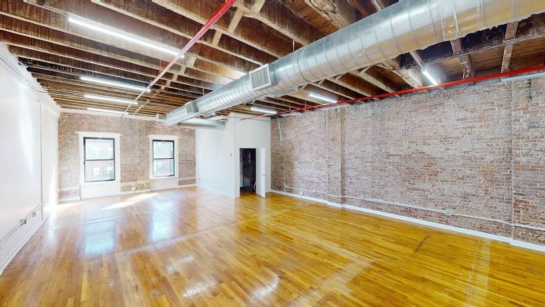 Empty loft space with exposed brick, beams, air ducts, and natural light.