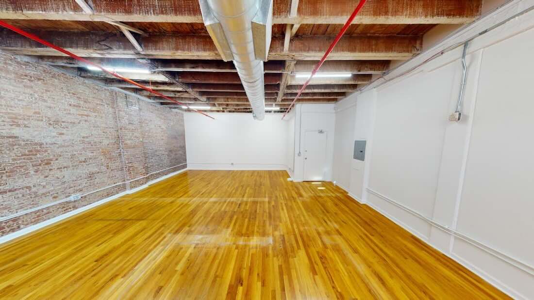 Room with wooden floors, brick walls, beams, and metal air ducts.