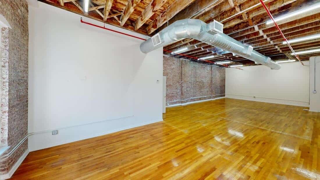 A spacious room with wooden floors, brick walls, and large windows.