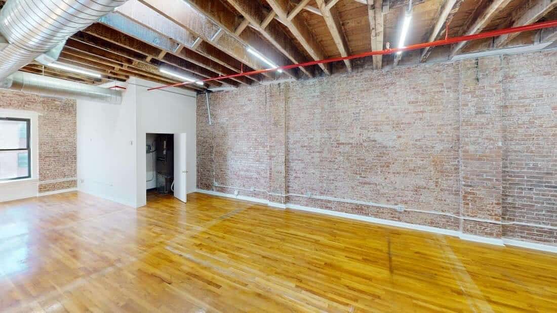 Room with brick wall, wooden floor, high ceiling, and large window.