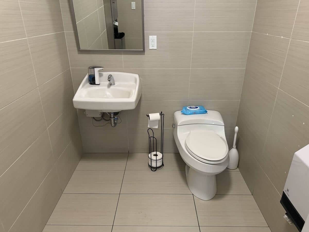 Clean bathroom with beige tiles, wall-mounted sink, toilet, and mirror.