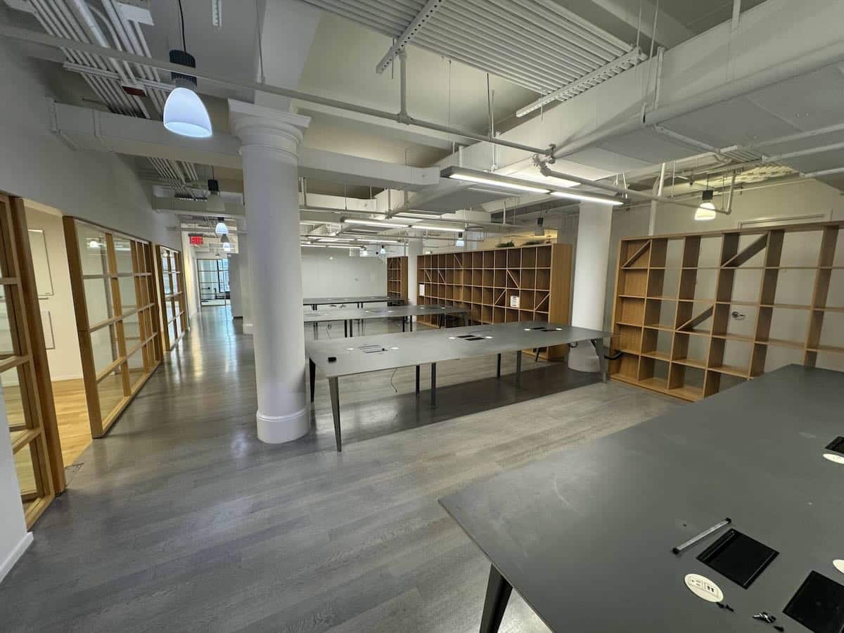 Modern office with open floor plan, tables, shelves & industrial lights.