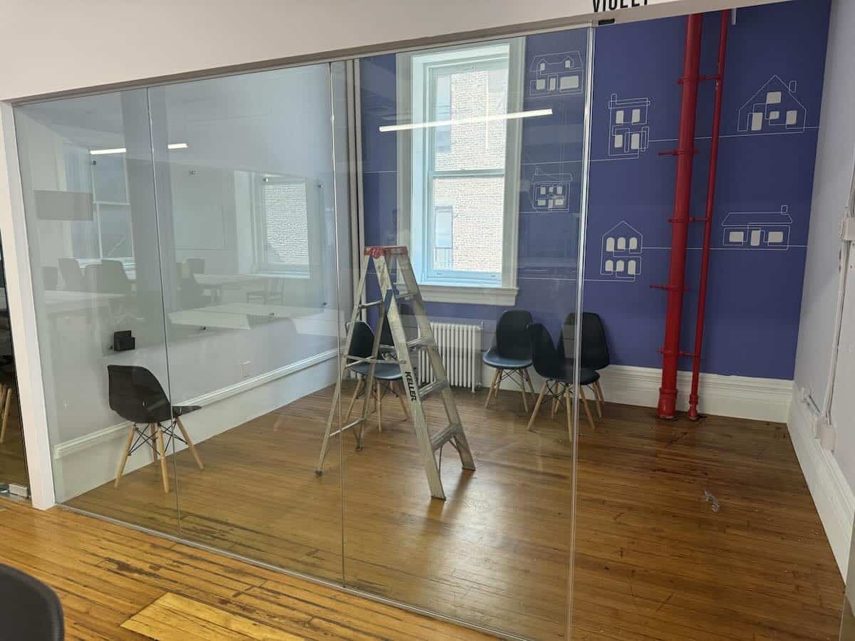 Meeting room with glass walls, black chairs, ladder, blue back wall.