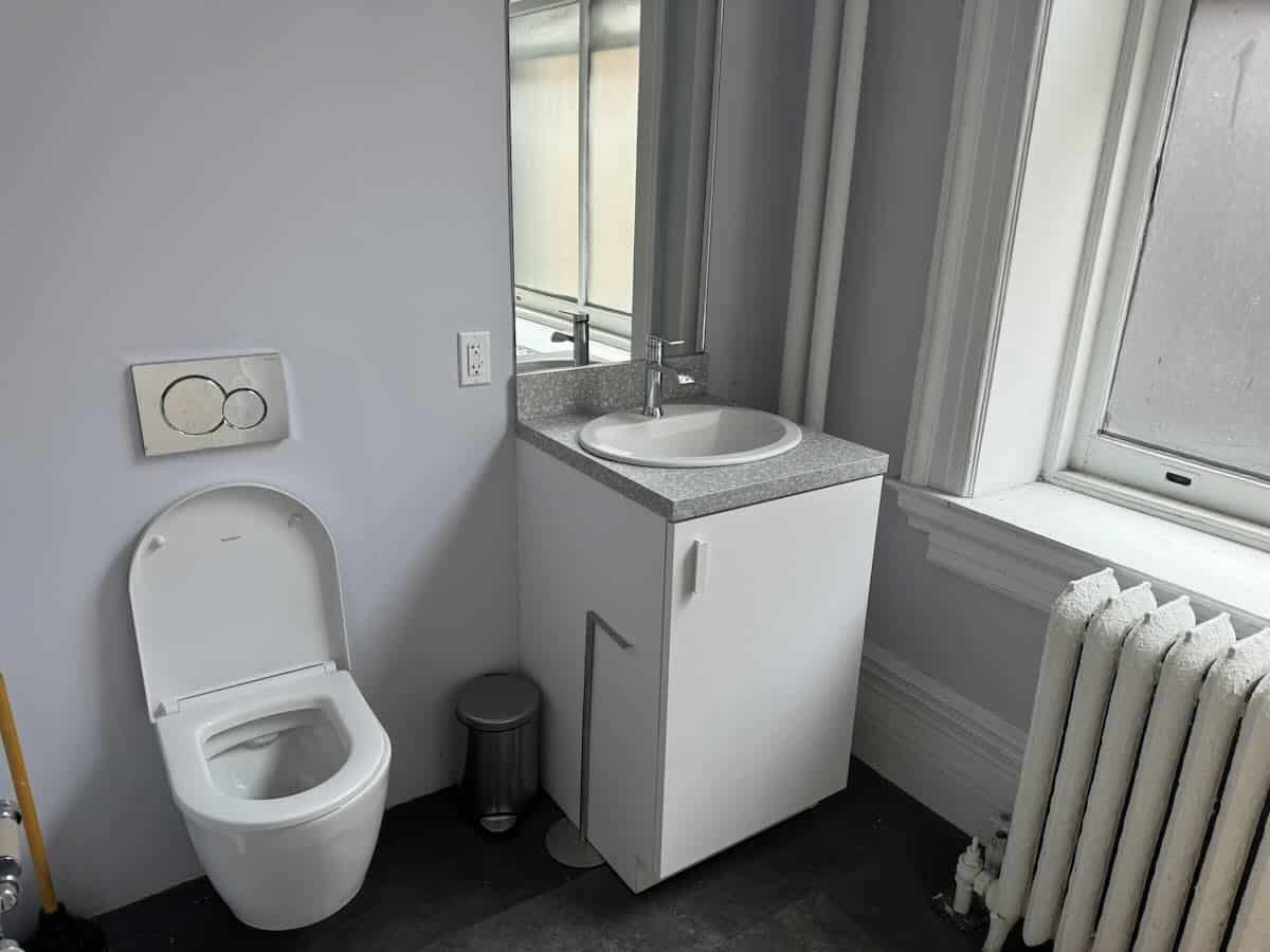 ALT: "Small bathroom on 4th floor with wall-mounted toilet and compact sink.