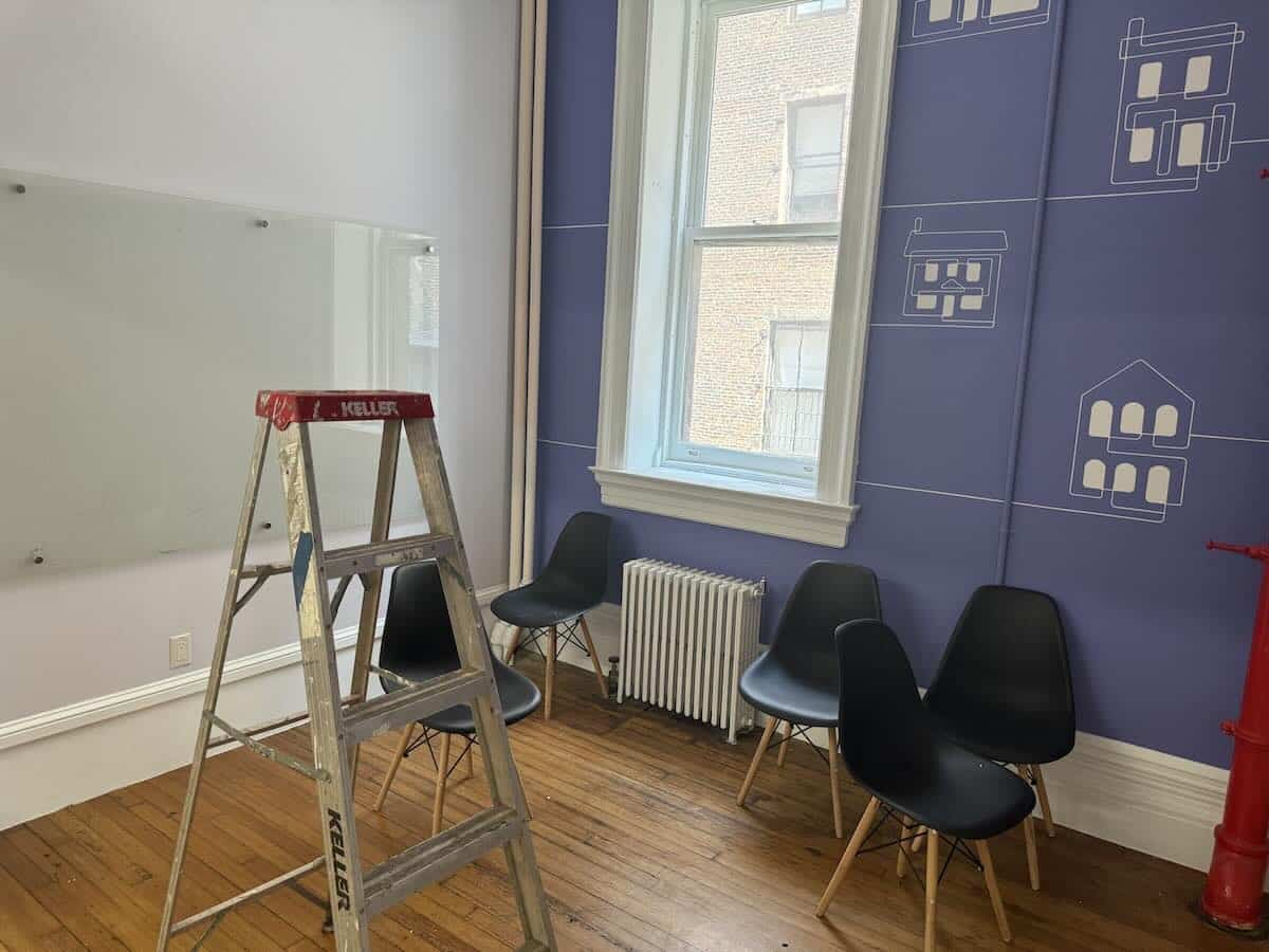 Room with wooden floor, black chairs, blue wall, ladder near window.