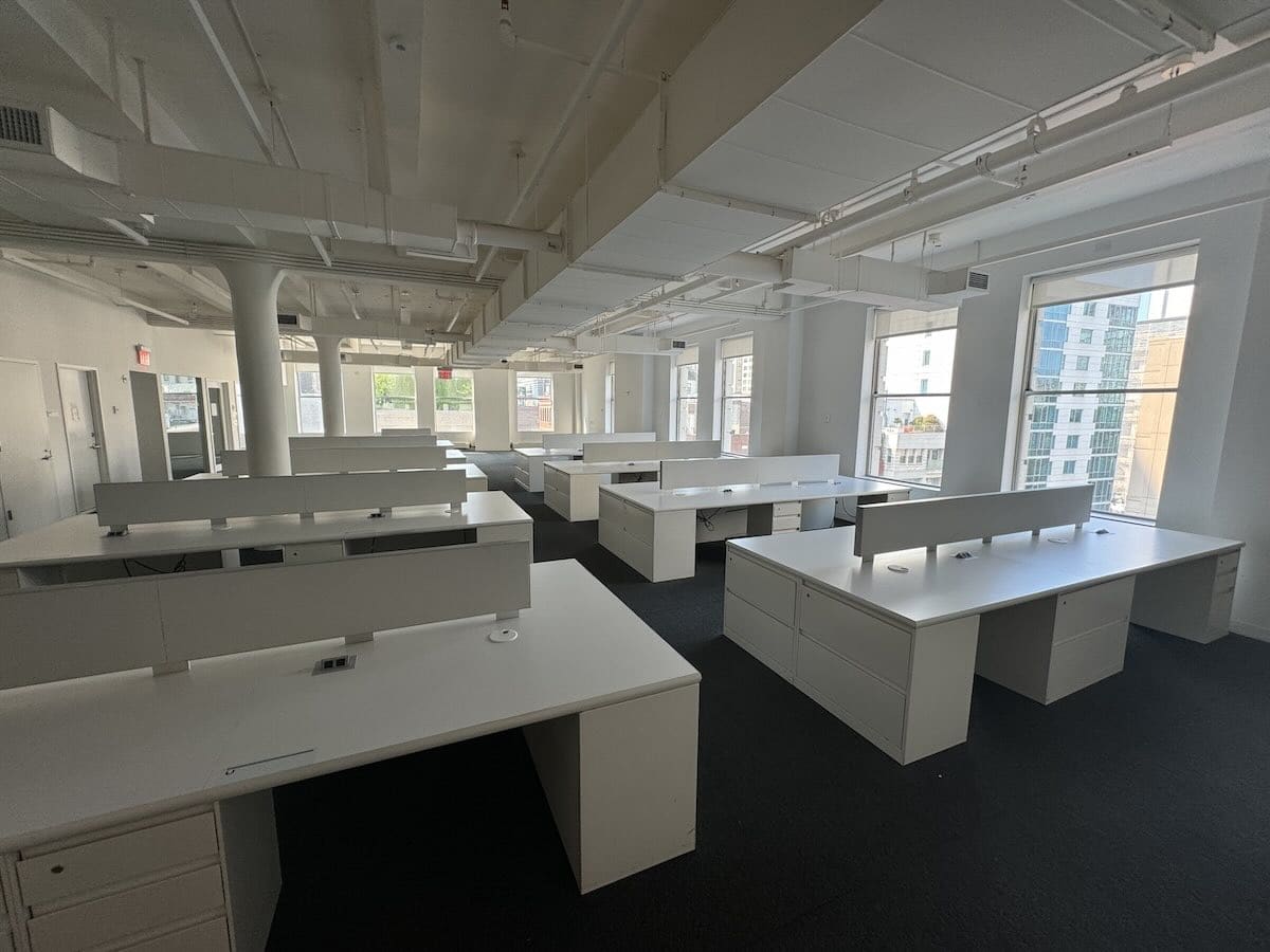 An empty, modern office space with several white desks and workstations.