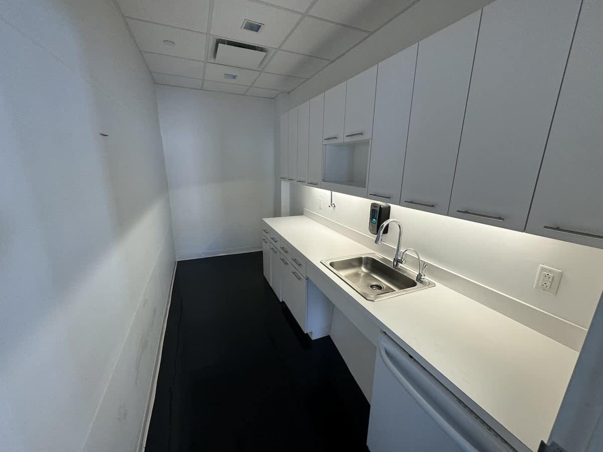 A narrow kitchen with white cabinets, stainless steel sink, and long countertop.