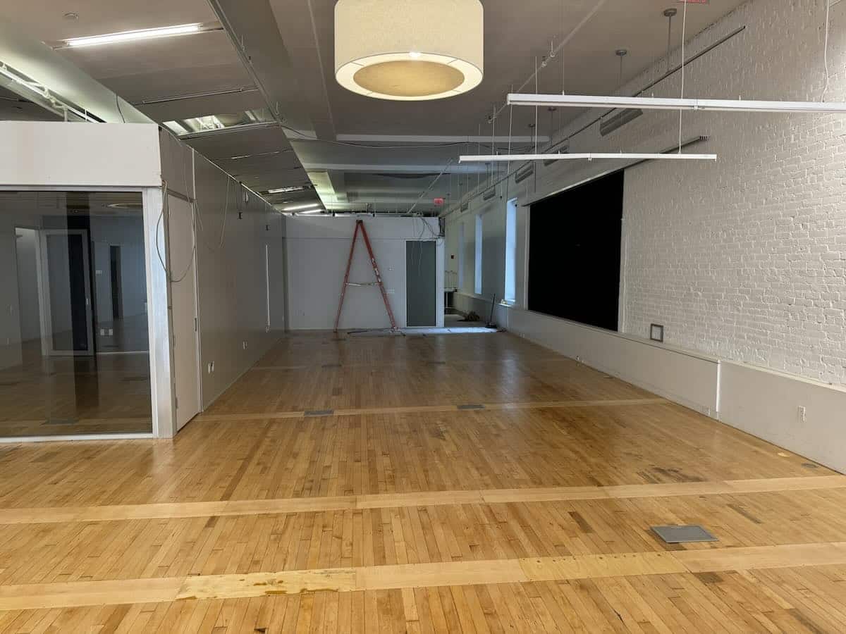 Empty room with wooden floors, red ladder, and large ceiling light.