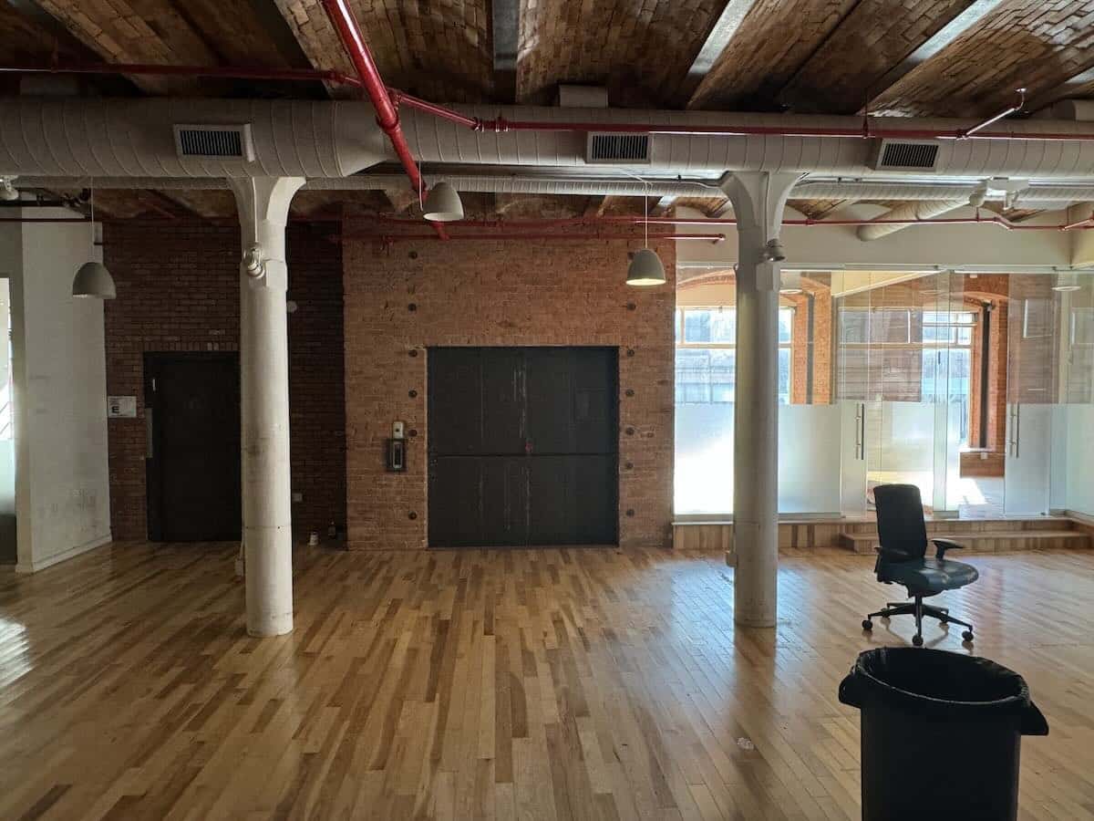 Exposed brick walls, wooden floors, and large windows in an industrial room.