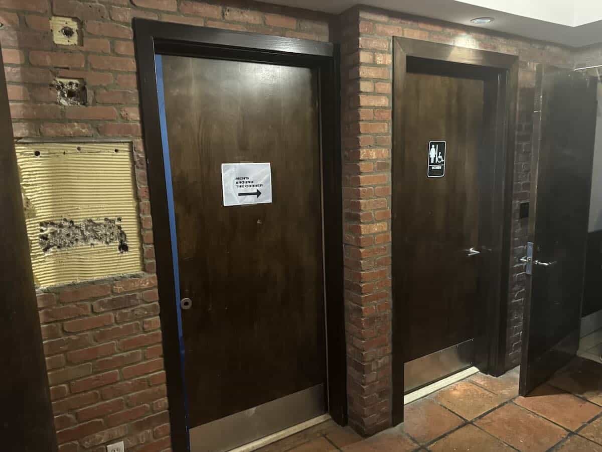 A dimly lit brick wall with two wooden doors, restroom signs.