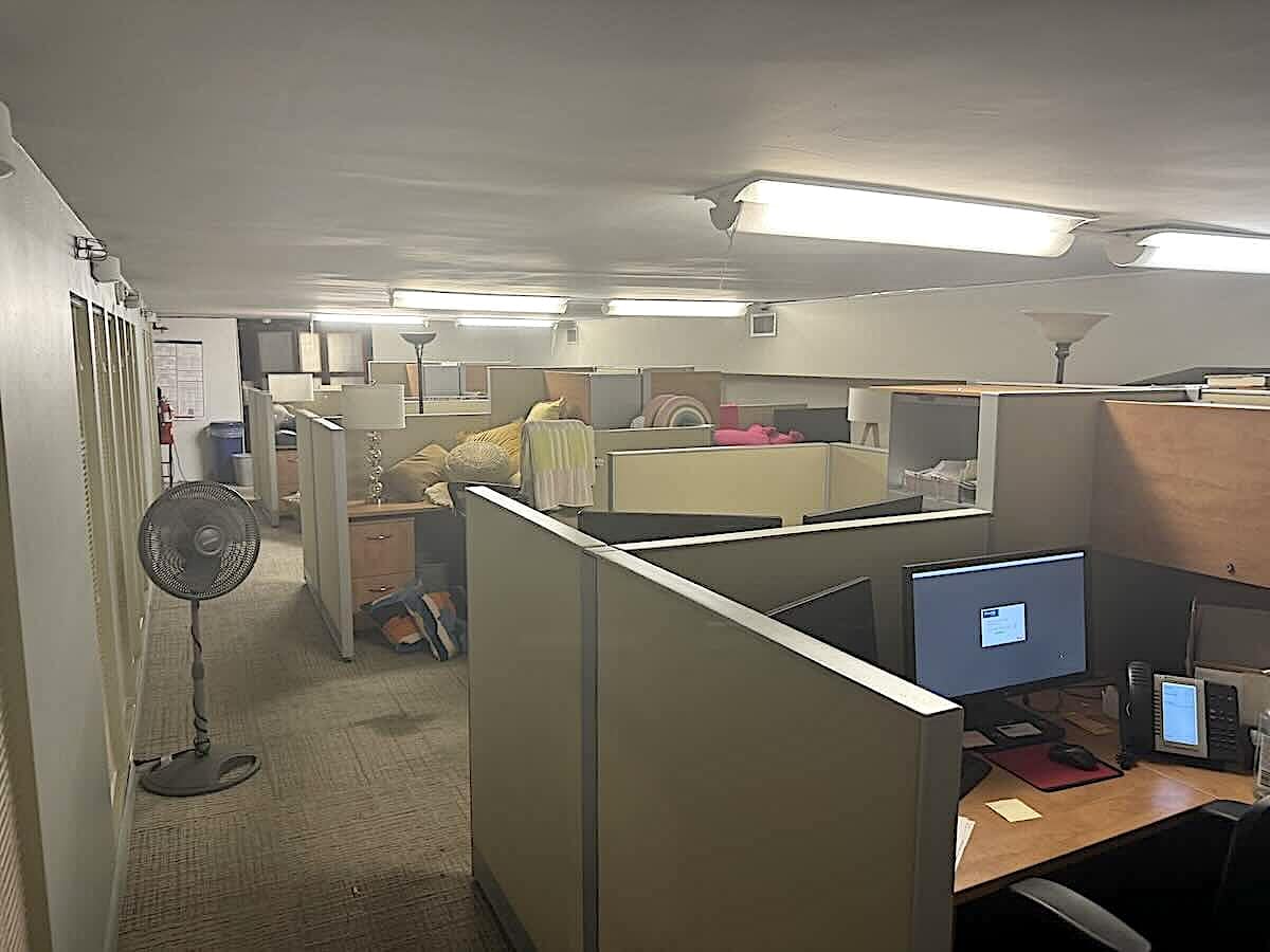 Ground-floor office with cubicles, desks, monitors, chairs, and supplies.