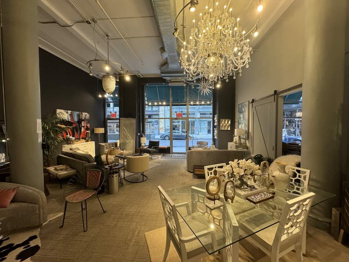 ```markdown
ALT: Modern furniture showroom with glass table, white chairs, and chandelier.