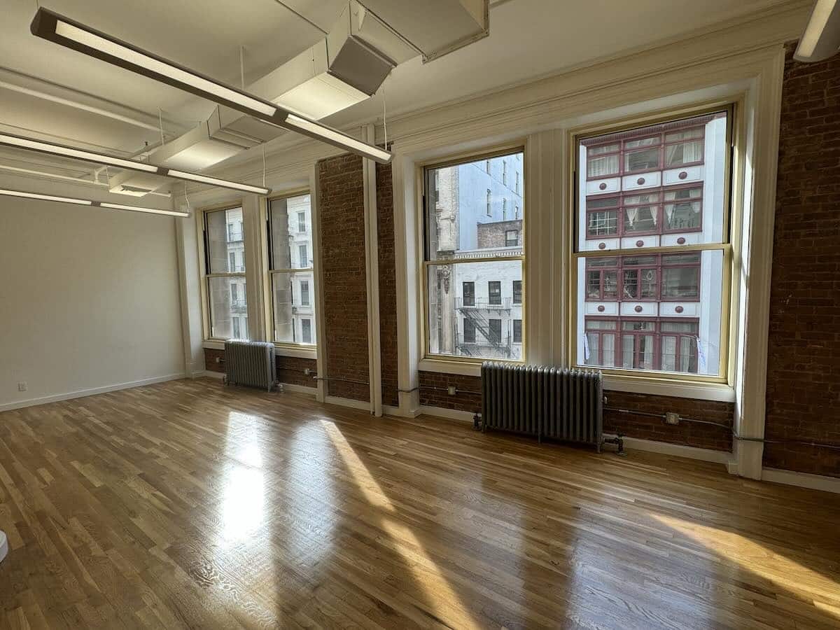 Sunlit room with large windows, wooden flooring, and exposed brick pillars.