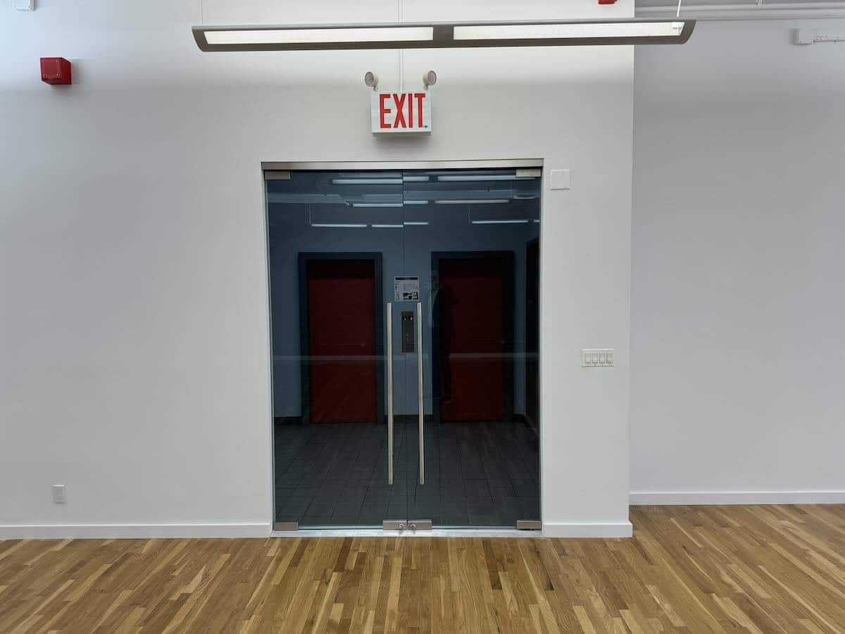 Modern interior with glass door, EXIT sign, wooden floor, white walls.