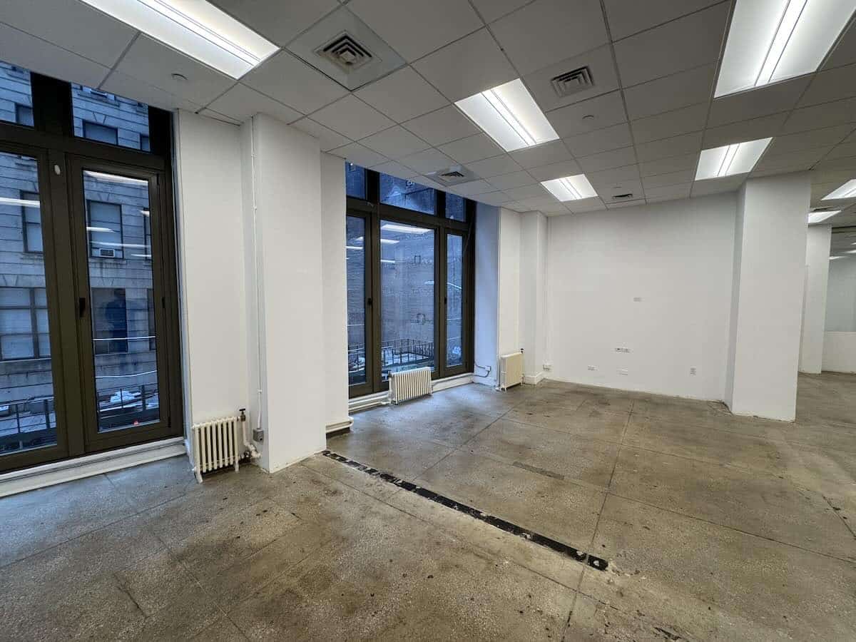 Empty office with large windows, white walls, and concrete floor