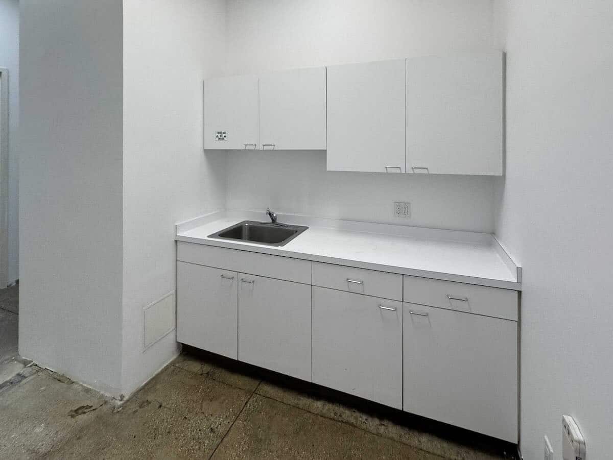 White kitchenette with cabinets, stainless steel sink, and light gray countertop.