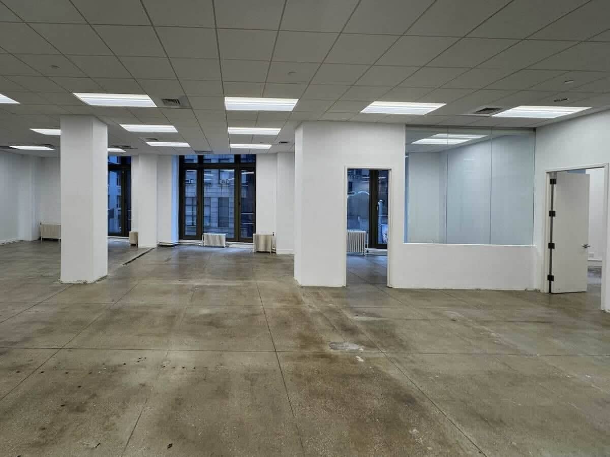 Spacious office with concrete floors, white walls, large windows.