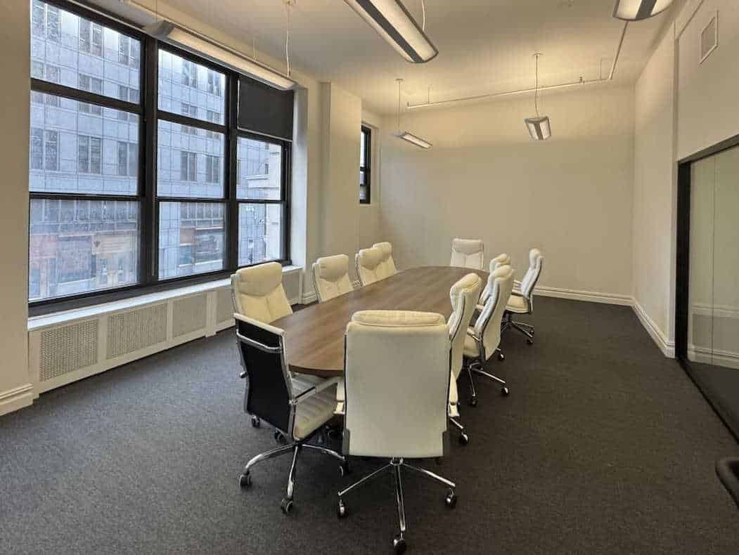 Office conference room with wooden table, white chairs, and large windows.