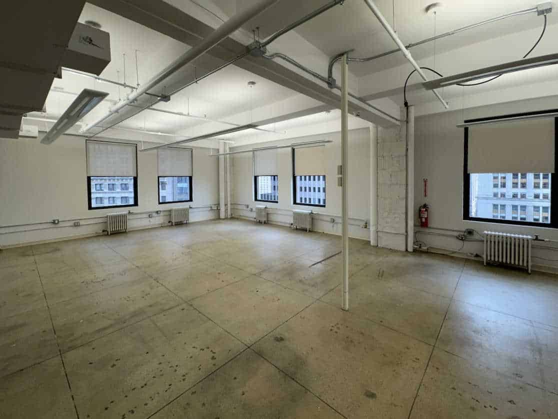 A large empty office with concrete floors, white walls, and big windows.