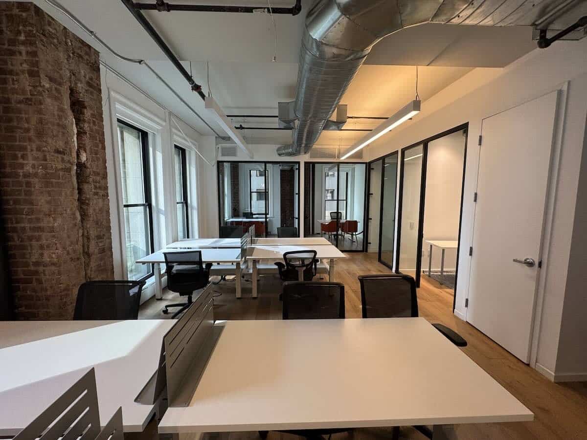 Modern office with white desks, black chairs, large windows and light wood floor.