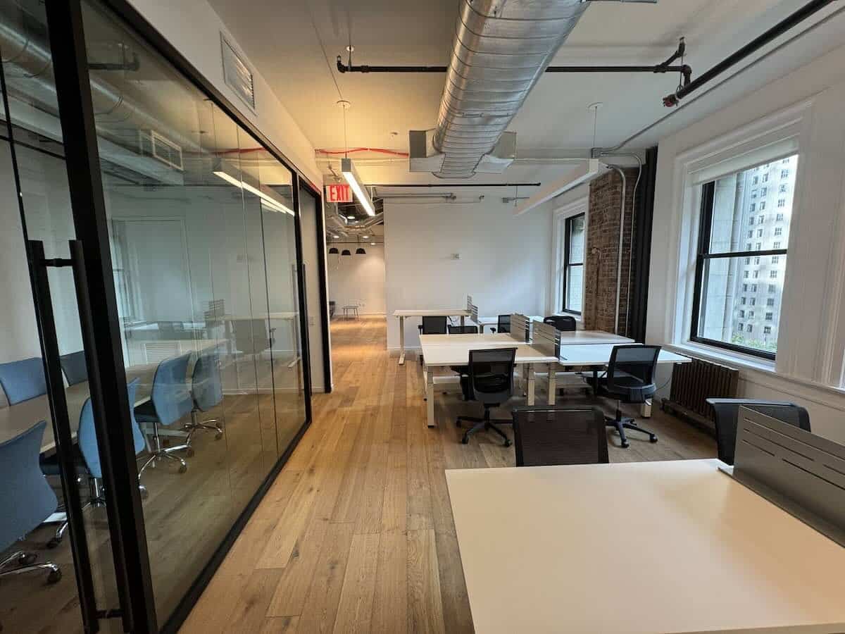 ALT text: Modern office at 703 Broadway with wooden floor, tables, and glass walls.