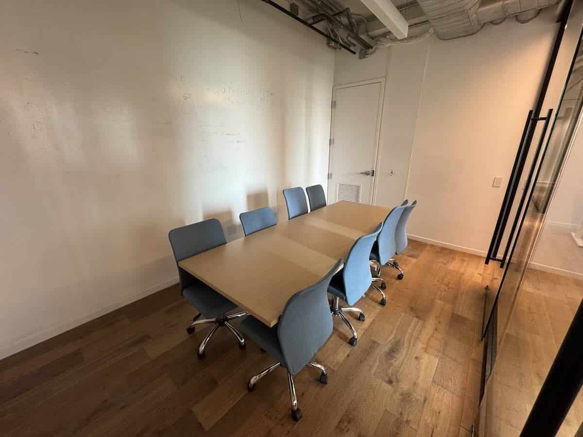 Minimalist conference room with wooden table and six blue chairs.