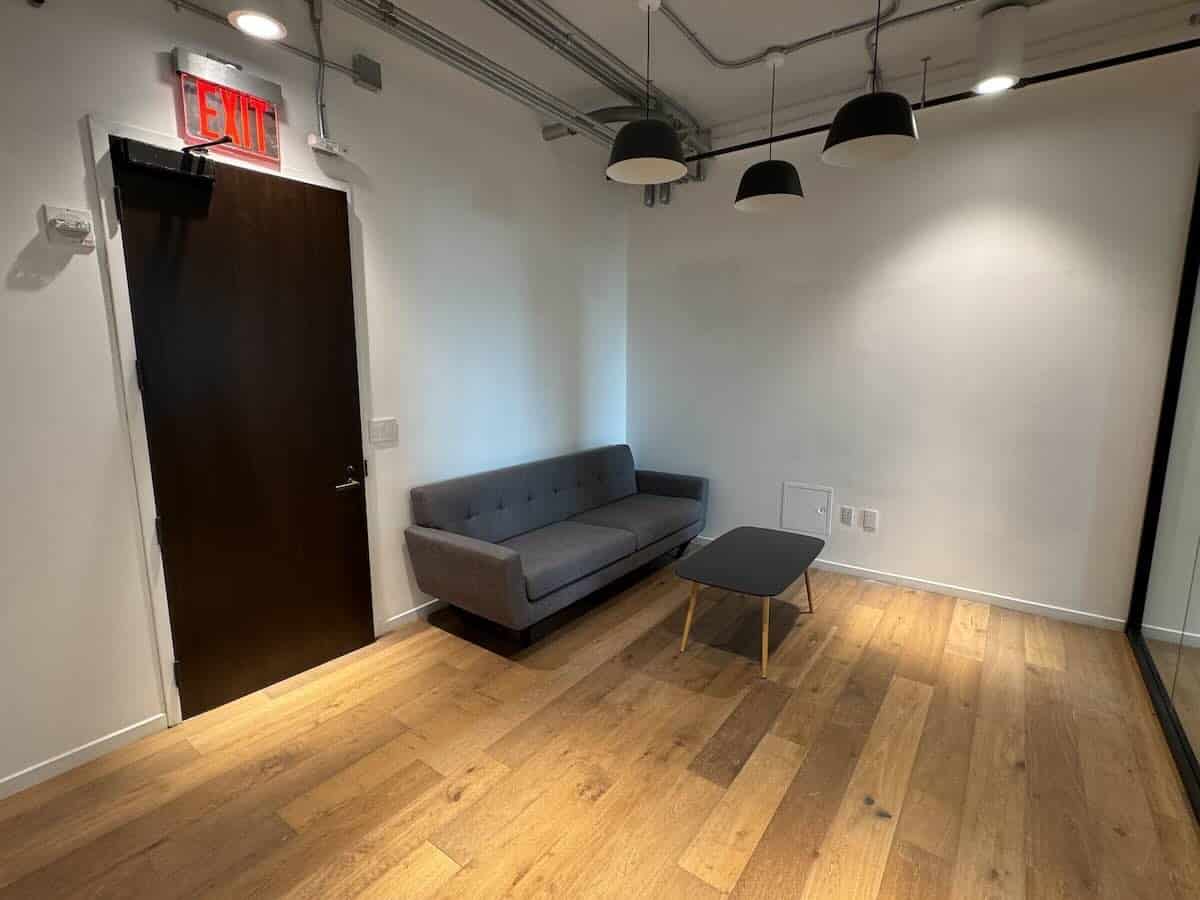 Minimalist office waiting area with sofa, coffee table, exit door, and industrial decor.