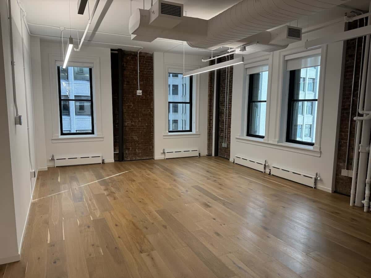 Bright room with hardwood floors, brick walls, and large windows.