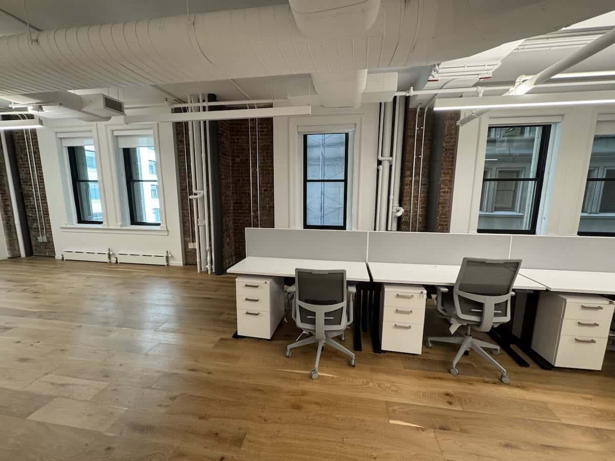 A modern office with wooden floors, white walls, and large windows.