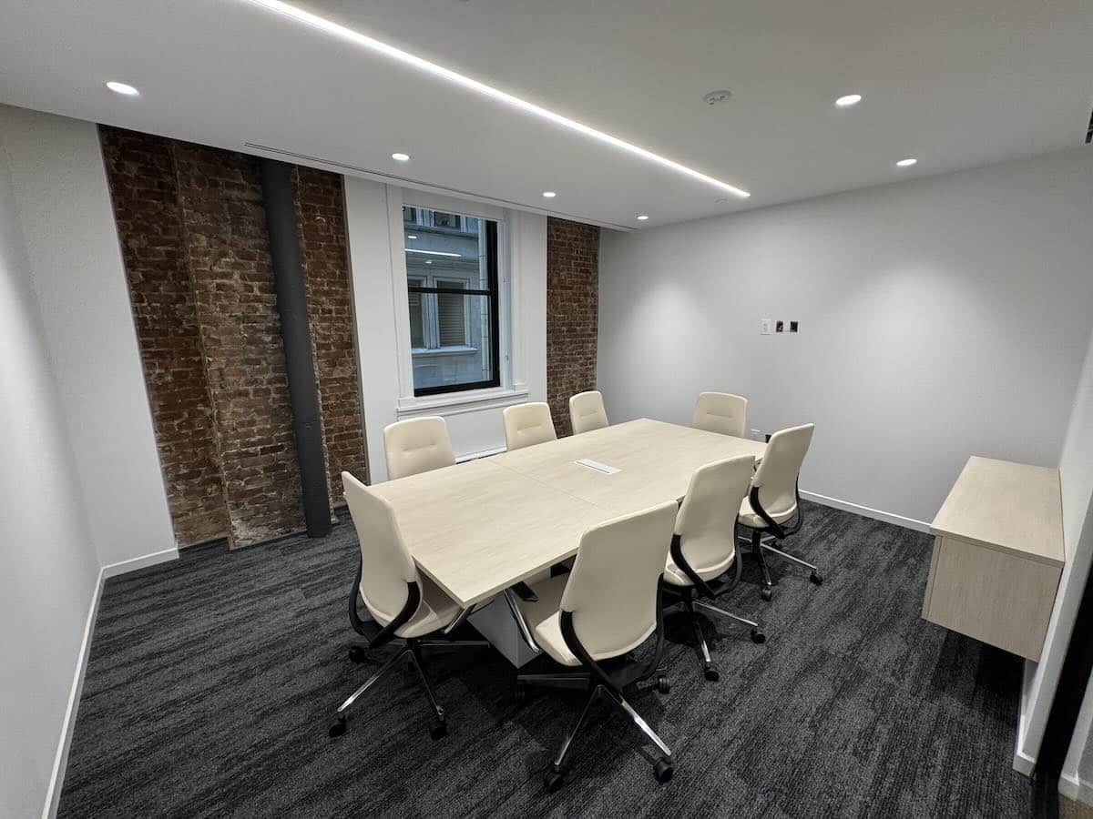 Modern conference room with table, chairs, brick walls, and natural light.