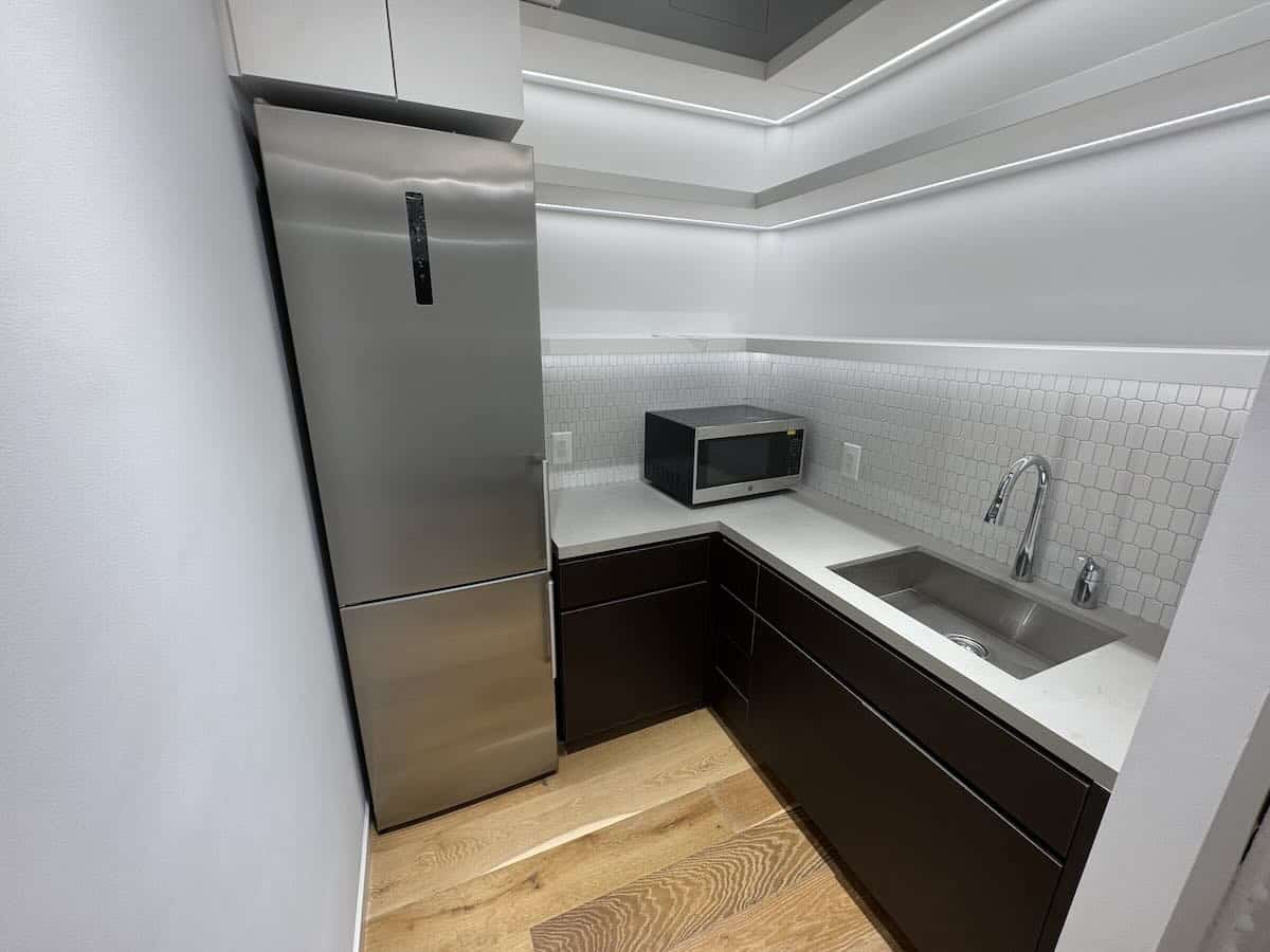 A modern kitchen with dark cabinets, white countertops, and wood floor.