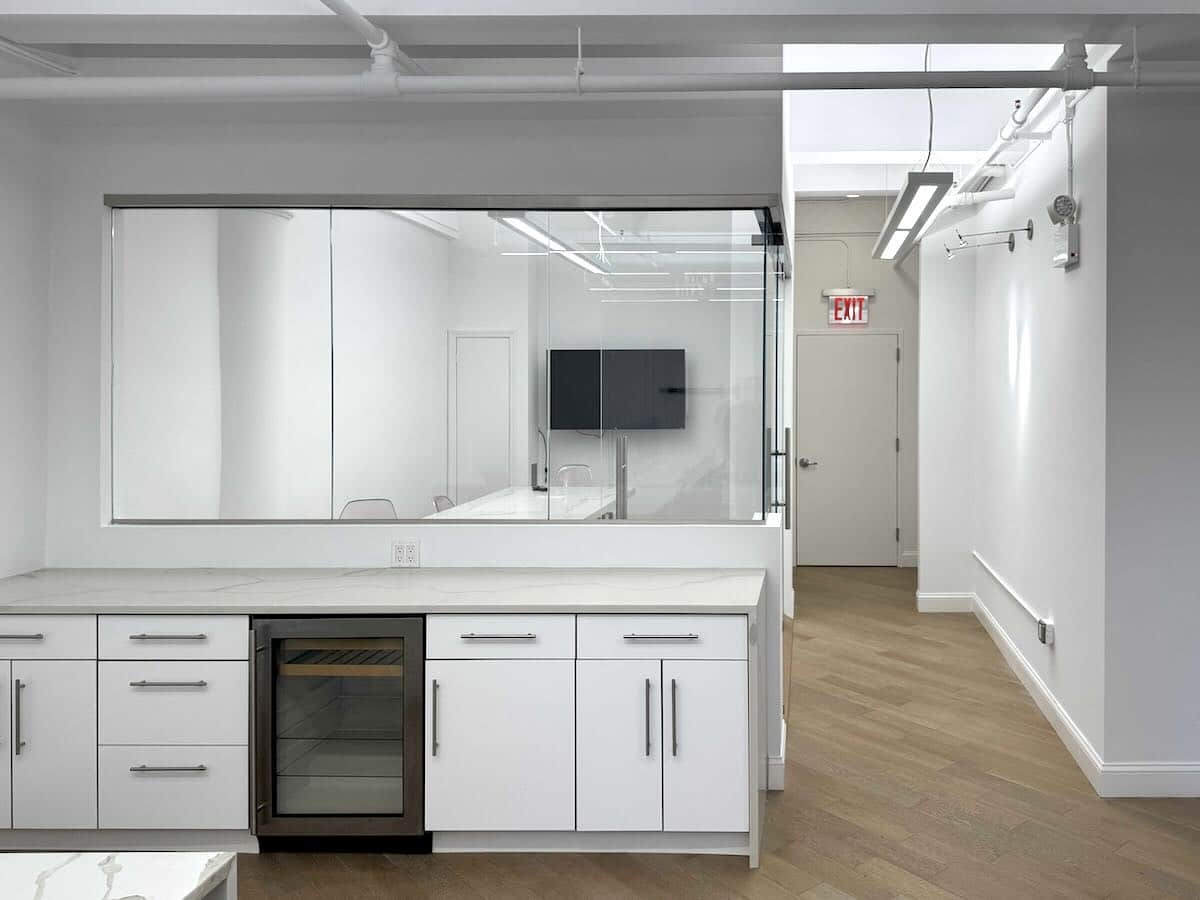 Modern office with glass conference room, white cabinetry, and wine cooler.