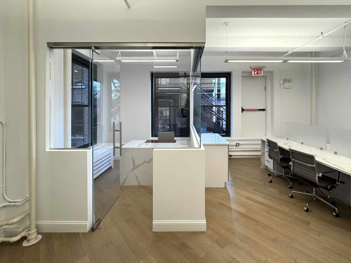 Modern office with wooden flooring, glass-walled room, office chairs and desks.