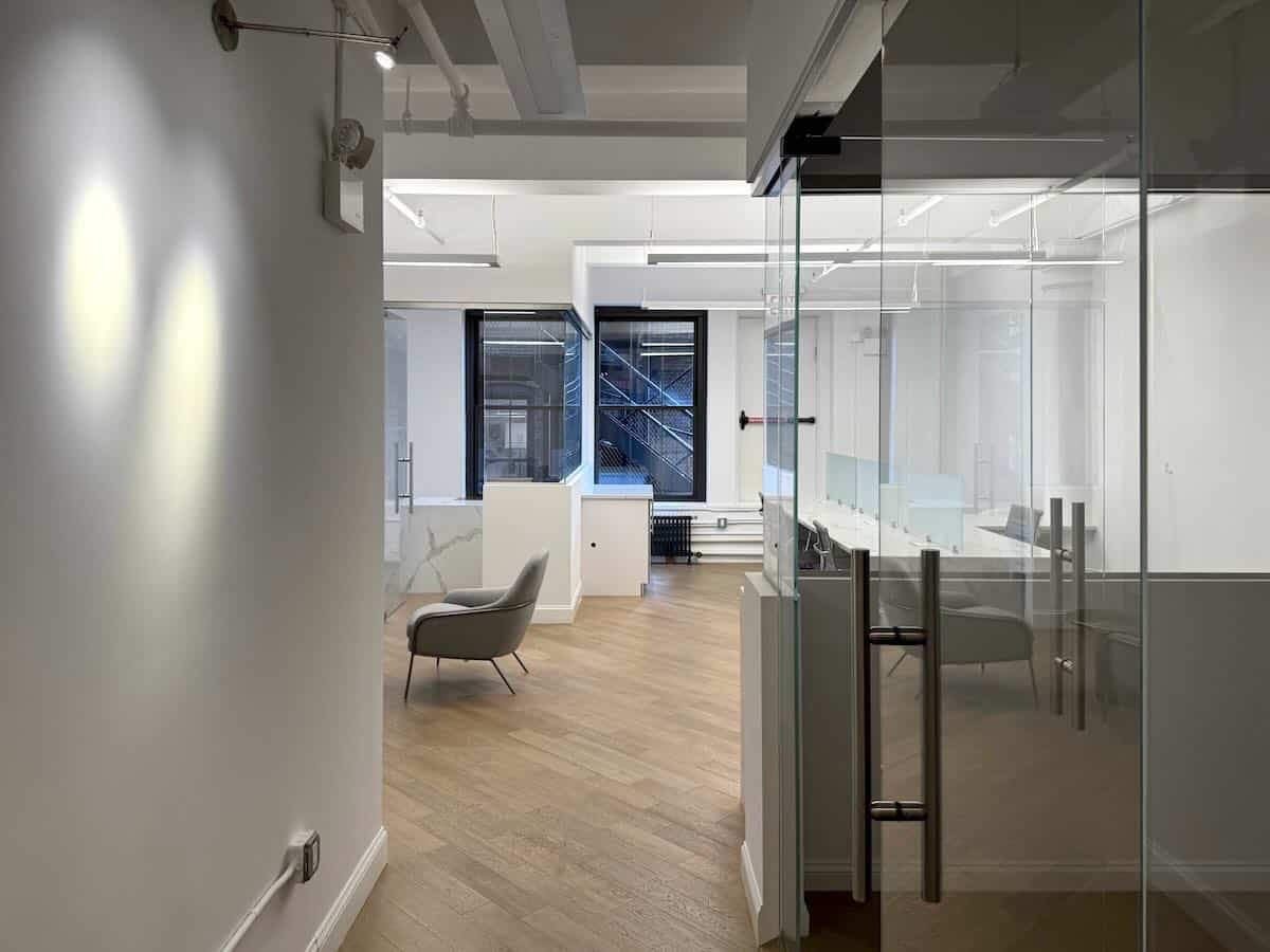 A minimalist office interior featuring white walls, glass partition room, wood floor and large windows,