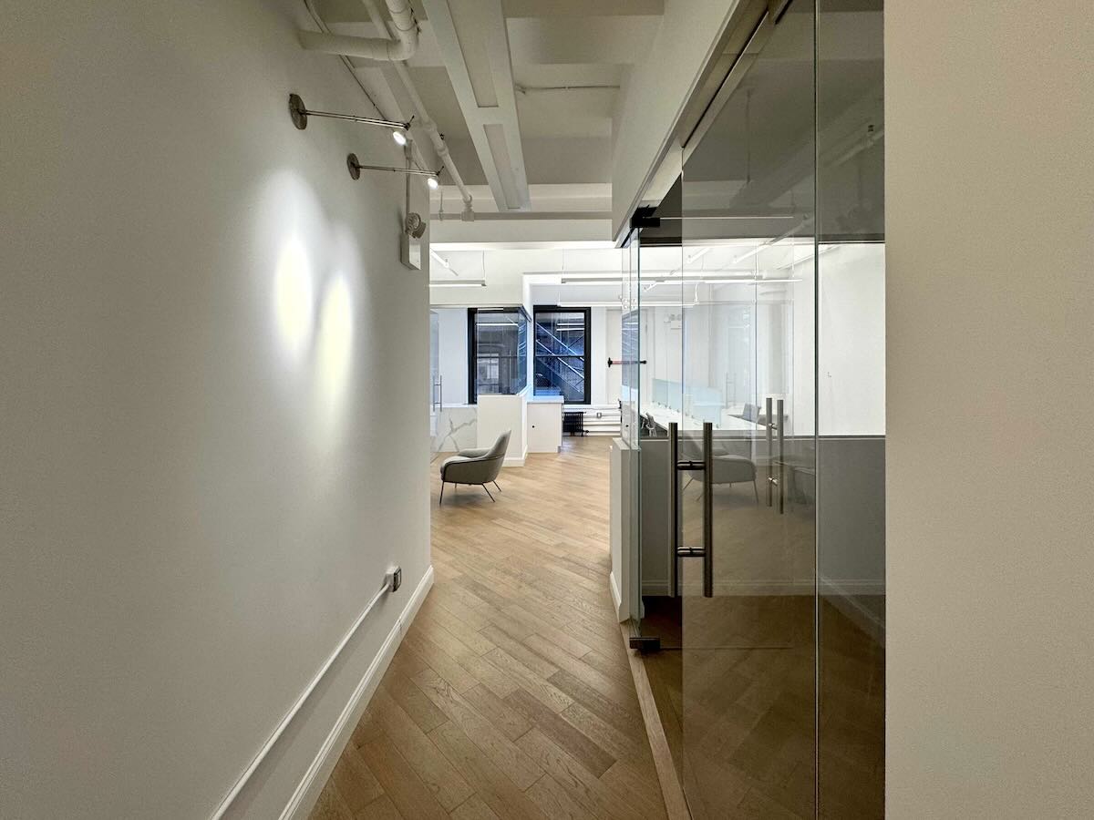 Modern office with wooden flooring, white walls, and glass partitions.