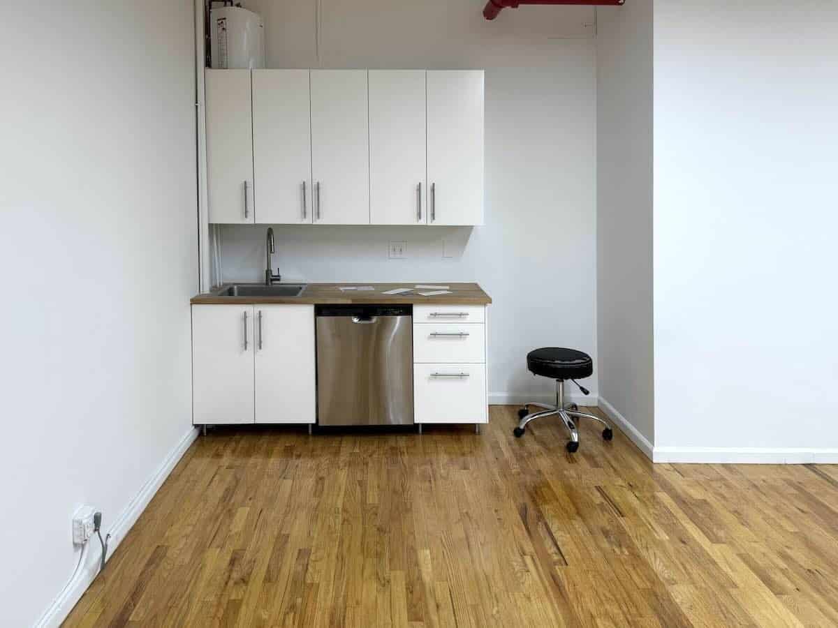 White kitchenette with wooden countertops and black stool on hardwood floor.