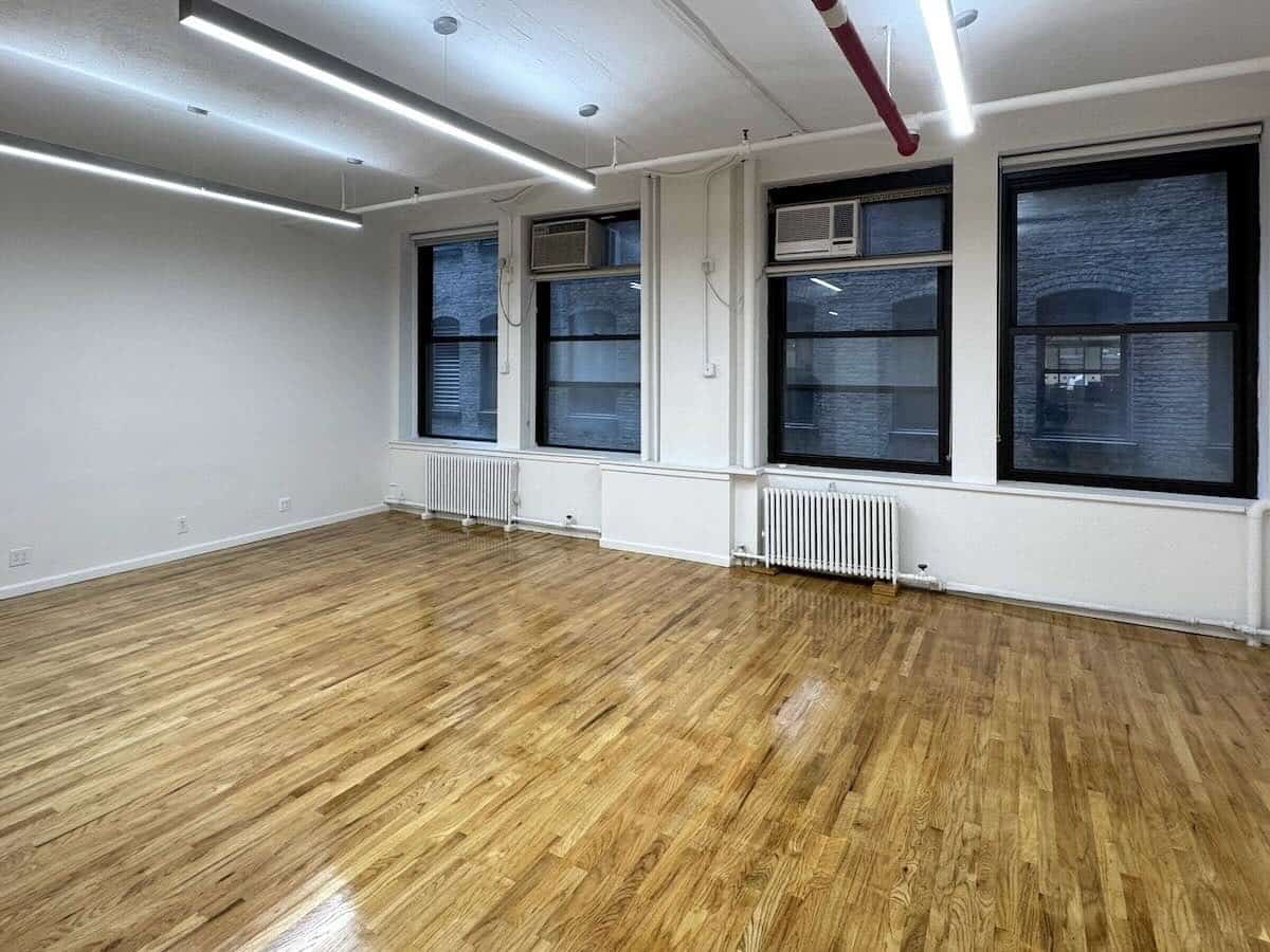 Empty room with wooden floors, white walls, and oversized windows.