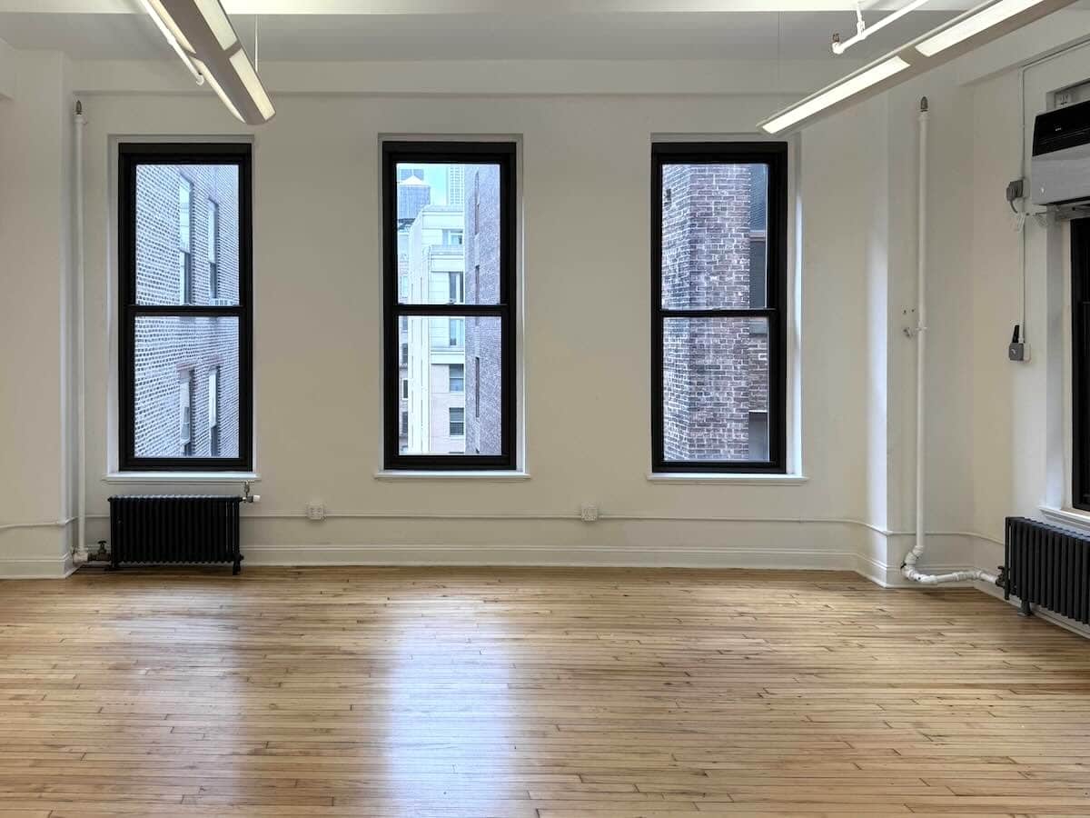 Spacious room with wooden floors, large windows, and white walls.