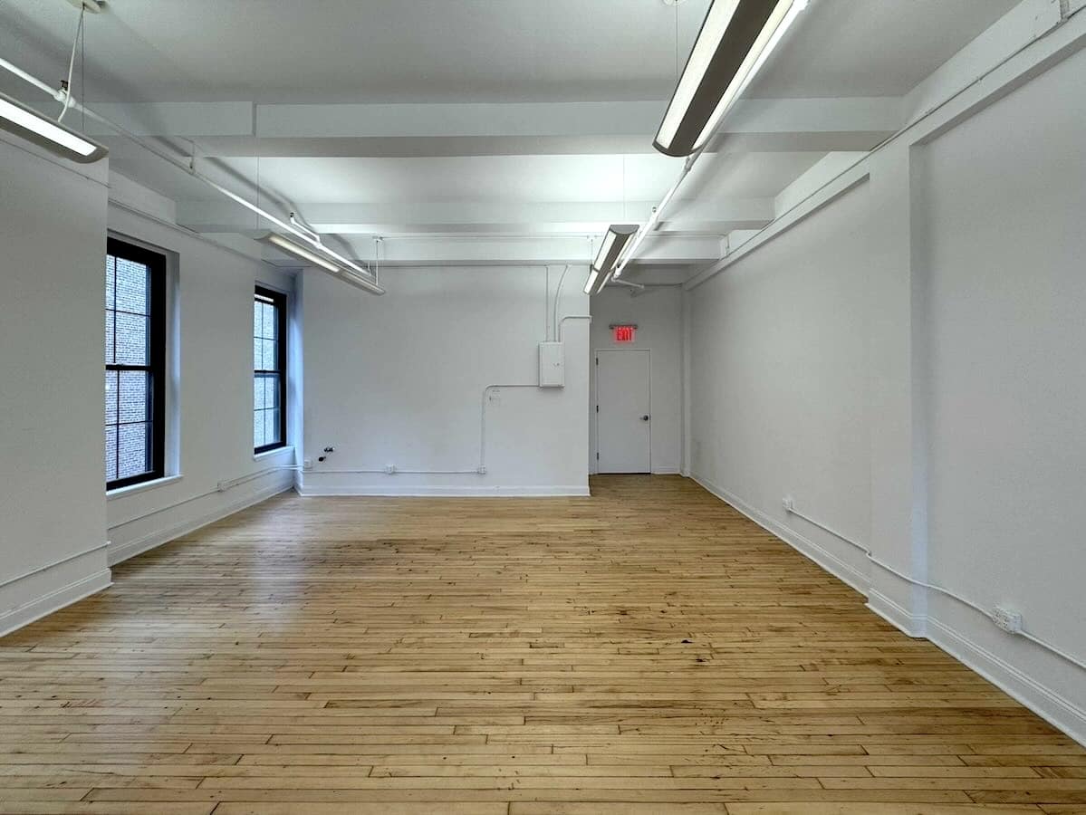 Bright room with wooden floors, white walls, and tall windows.