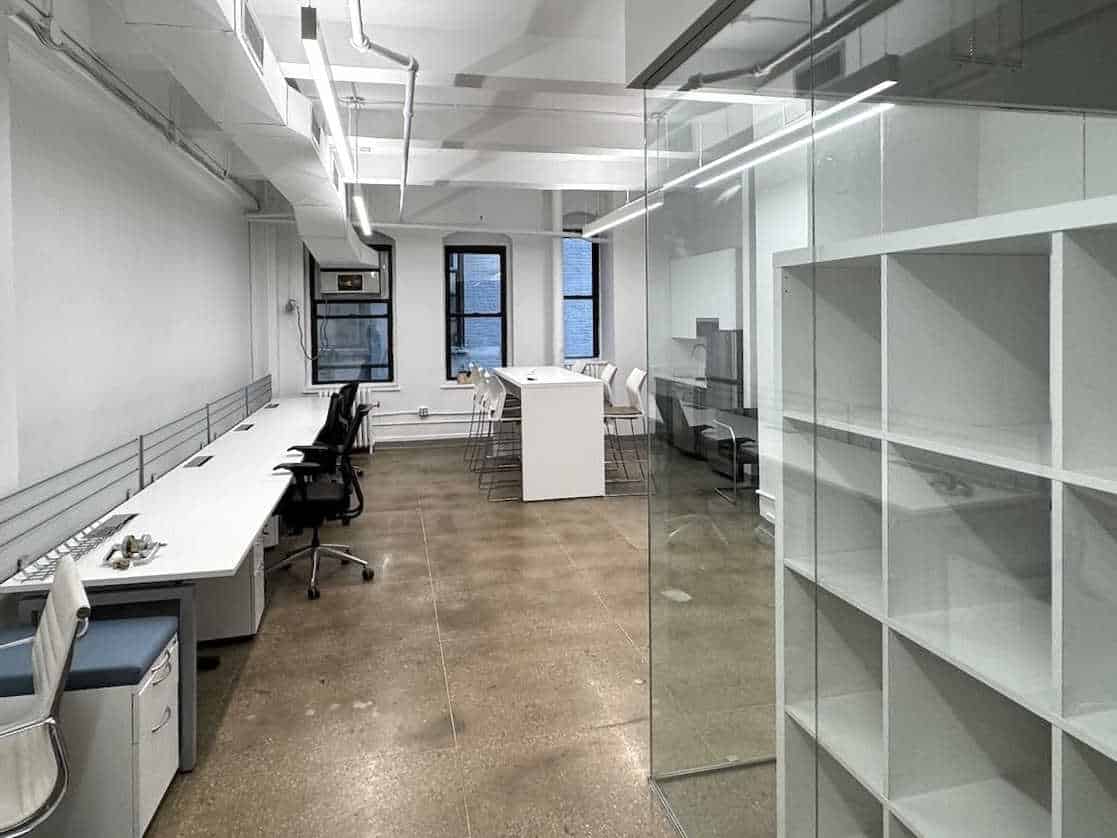 Modern office with white desk, chairs, shelves, and large windows.