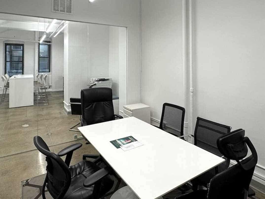 A modern office conference room with white table and black chairs.