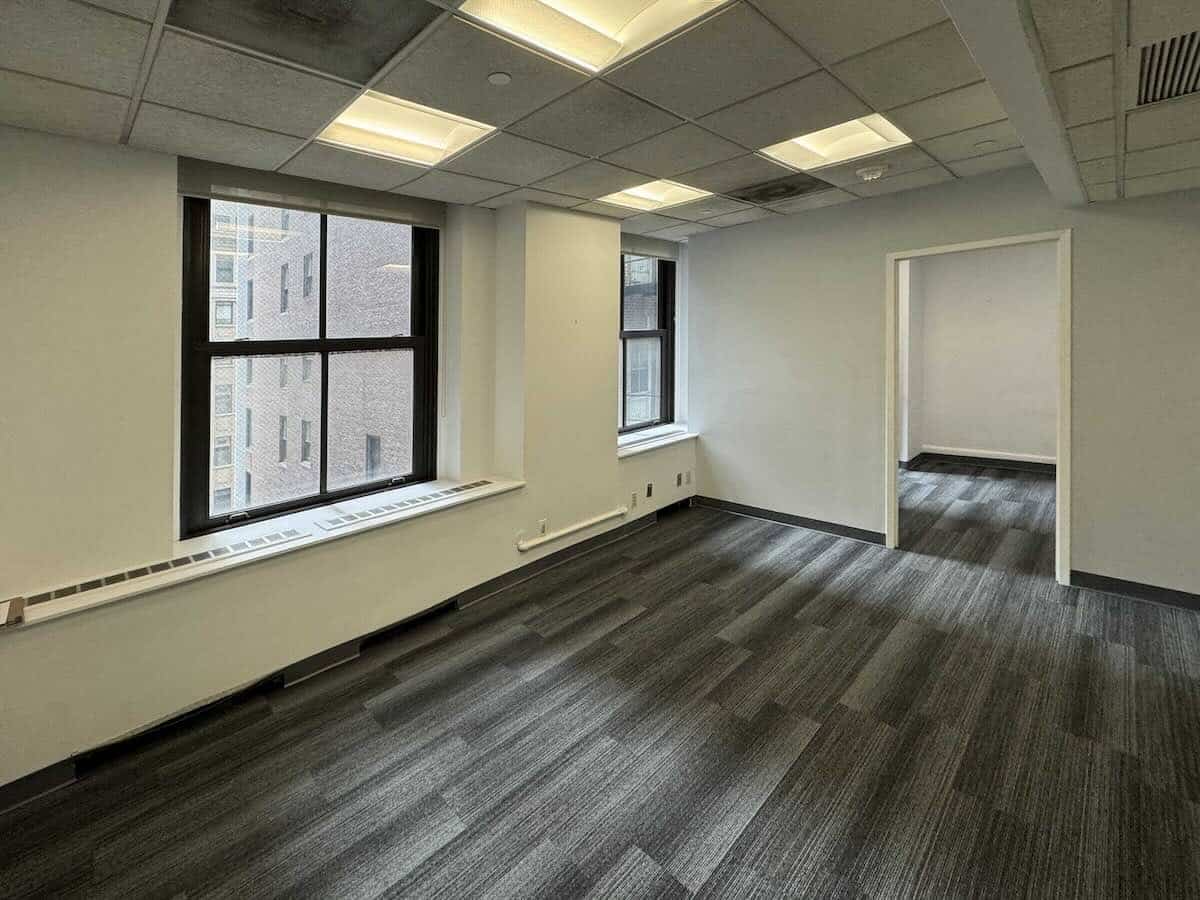 Empty office space with gray carpet, white walls, and large windows.