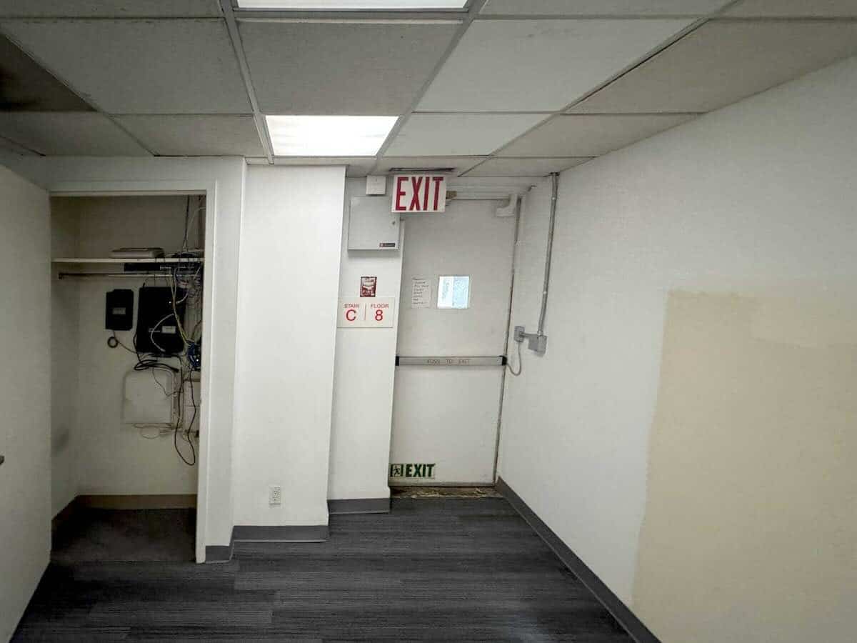 A room with white walls, ceiling tiles, and an open closet with equipment.