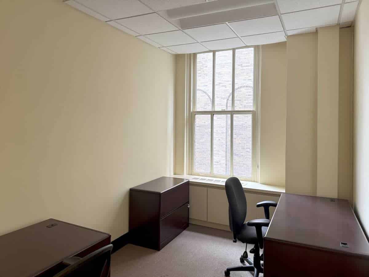 A small office with cream walls, window light, and two wooden desks.